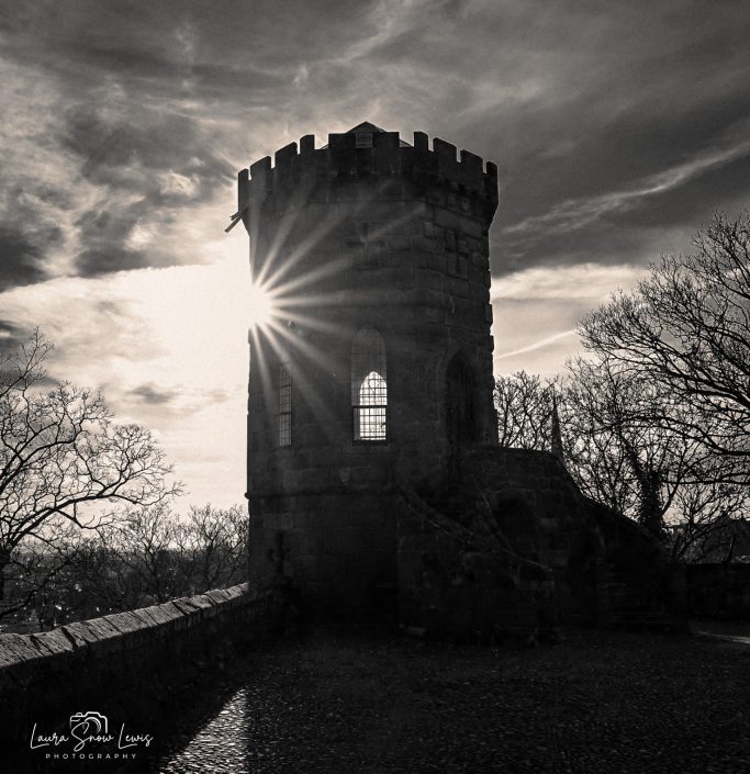 Silhouette of a tower against a dramatic sky with sunlight shining through a window.