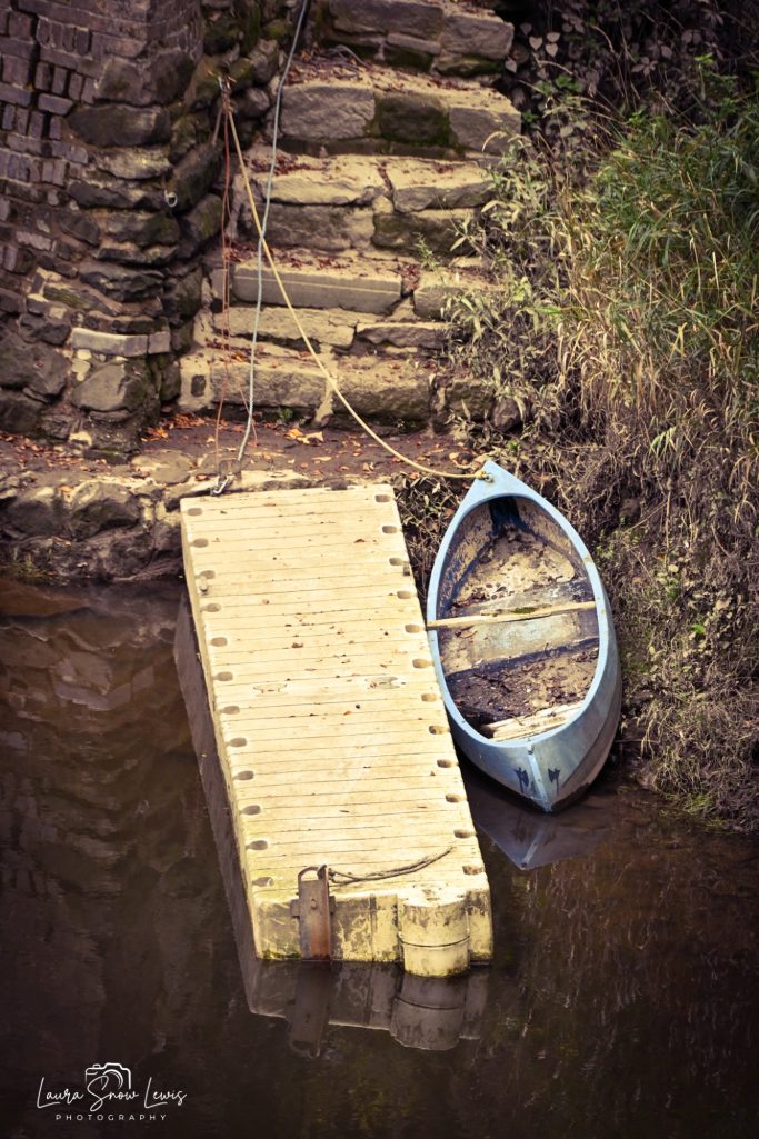A blue boat rests beside a wooden dock and stone steps by a calm waterway.