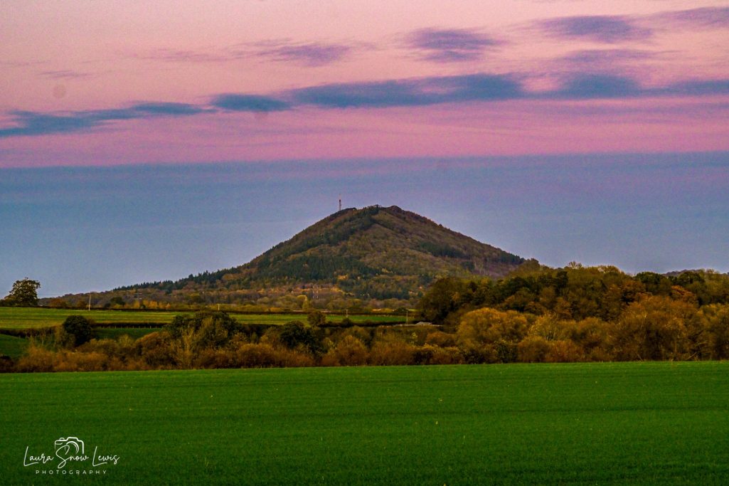 Landscape featuring a conical hill against a vibrant sunset sky.