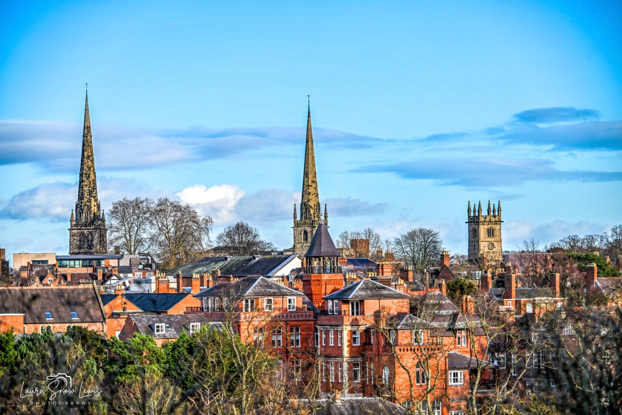 View of Shrewsbury town with notable spires and red-brick buildings under a blue sky.