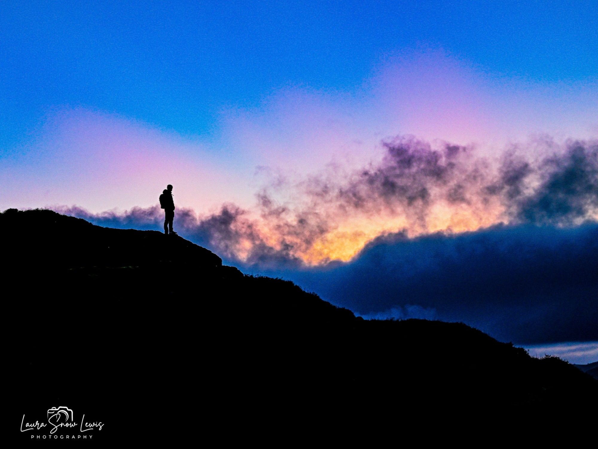 Silhouette of a person standing on a rocky outcrop against a colourful sunset sky. Caradoc, Church Stretton