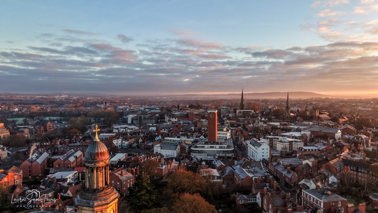 Panoramic view of a city skyline at sunrise, showcasing buildings and a cloudy sky.