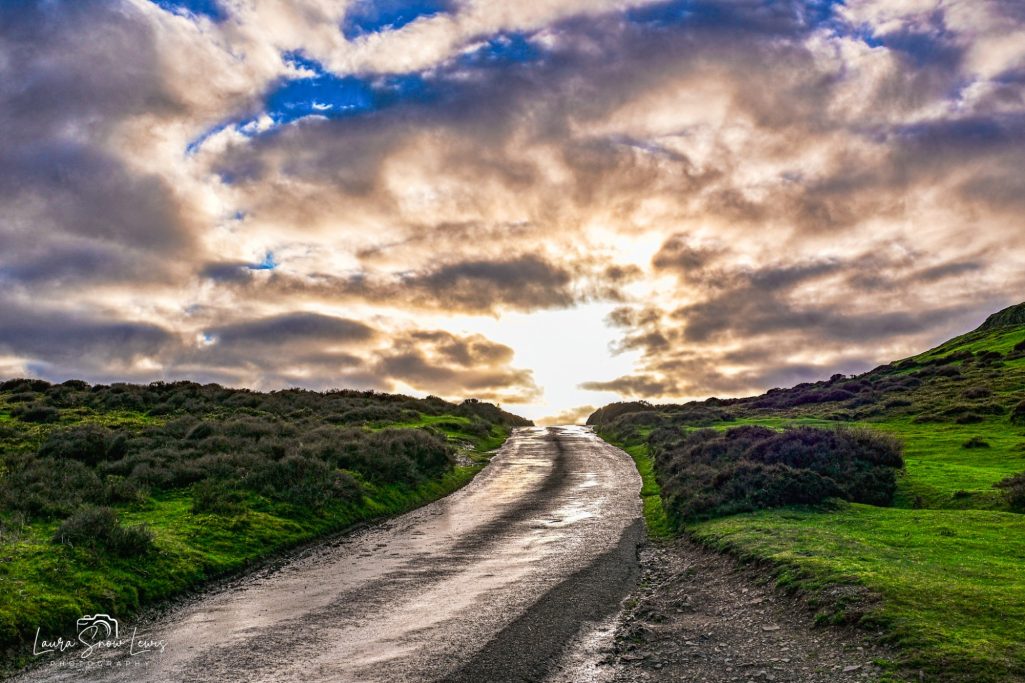 A winding road leading towards a bright horizon under a cloudy sky.